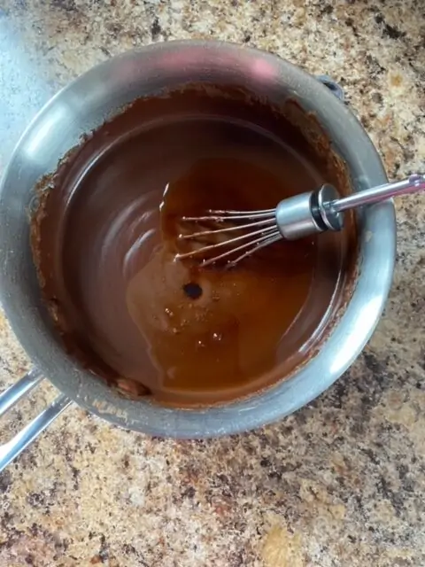 Chocolate sauce in a small saucepan with a whisk.