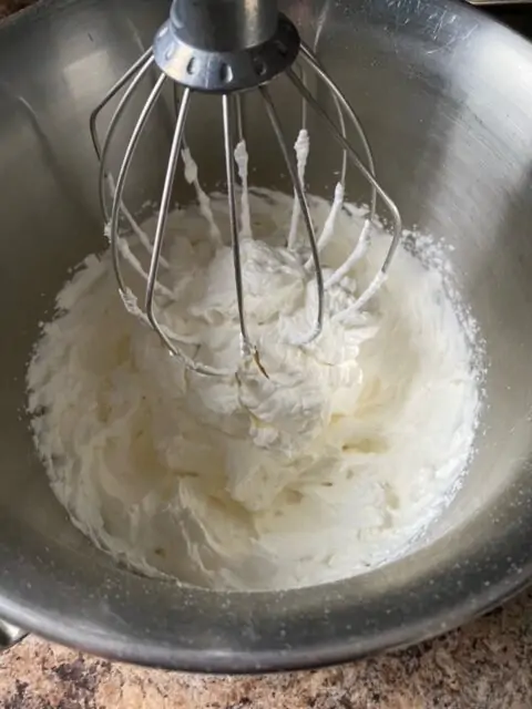 Whipped cream in a bowl of an electric mixer with the whisk attachment.