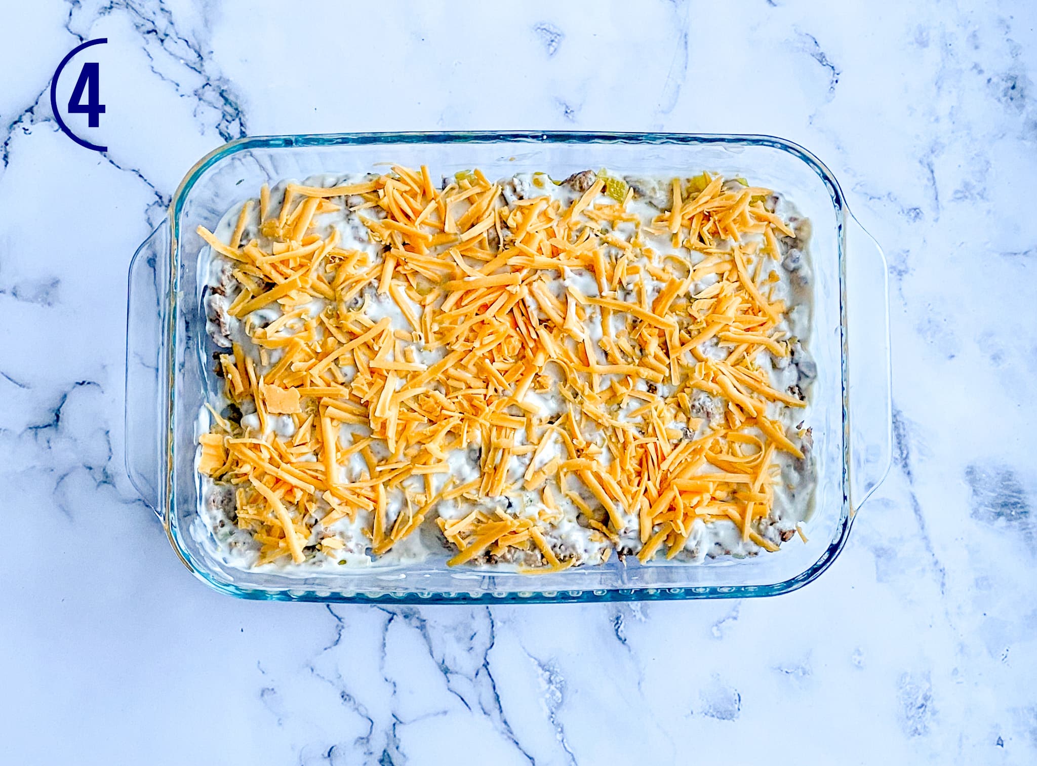The casserole is topped with cheddar cheese, which is scattered on top of the creamy sauce.