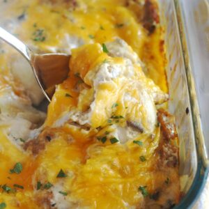 Pierogi casserole in a clear baking dish. A spoon is scooping up a spoonful of casserole.