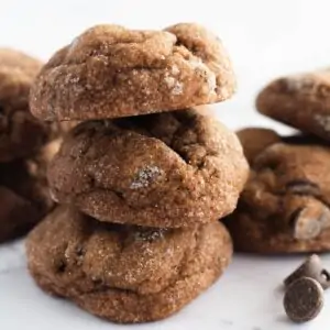 Cookies stacked on top of each other. Some chocolate chips are scattered around them.