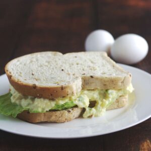 An intact sandwich on a white plate. Two eggs are in the background.
