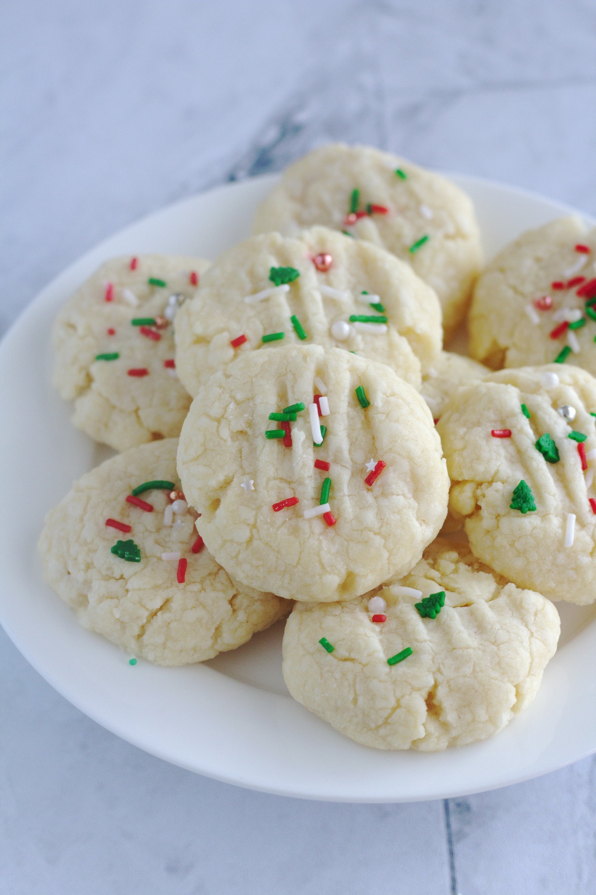 Cookies with red and green sprinkles on top, sit on a white plate.