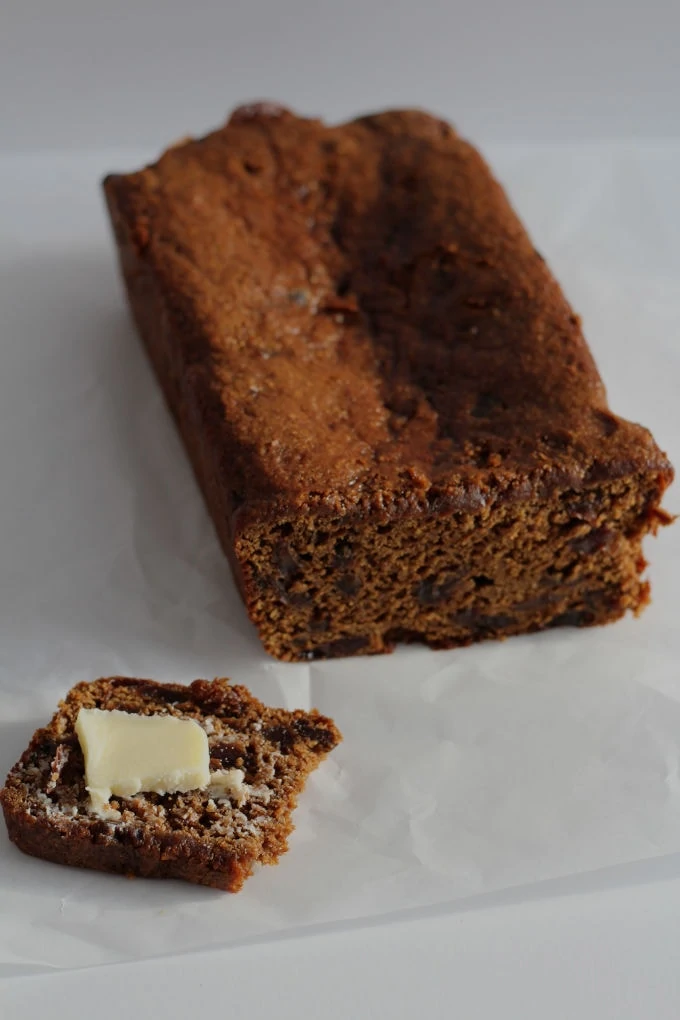 A loaf of malt bread with a small slice cut from it that has butter on top.