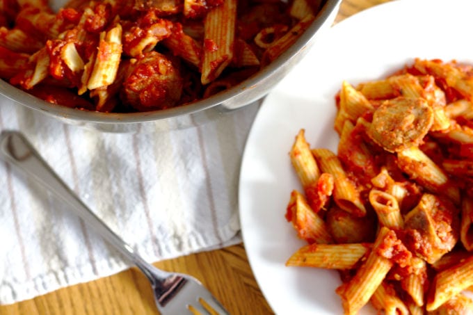 Pasta on a white plate with a fork beside it.  A pan with the rest of the pasta is also beside it.