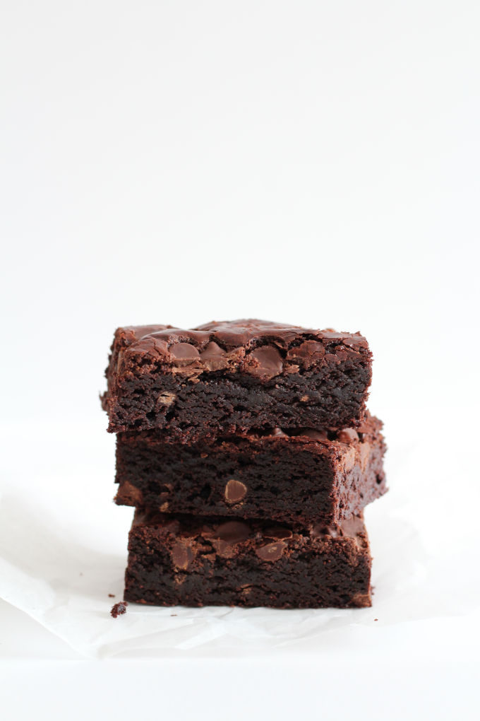 Three fudge brownies stacked on a piece of parchment paper.