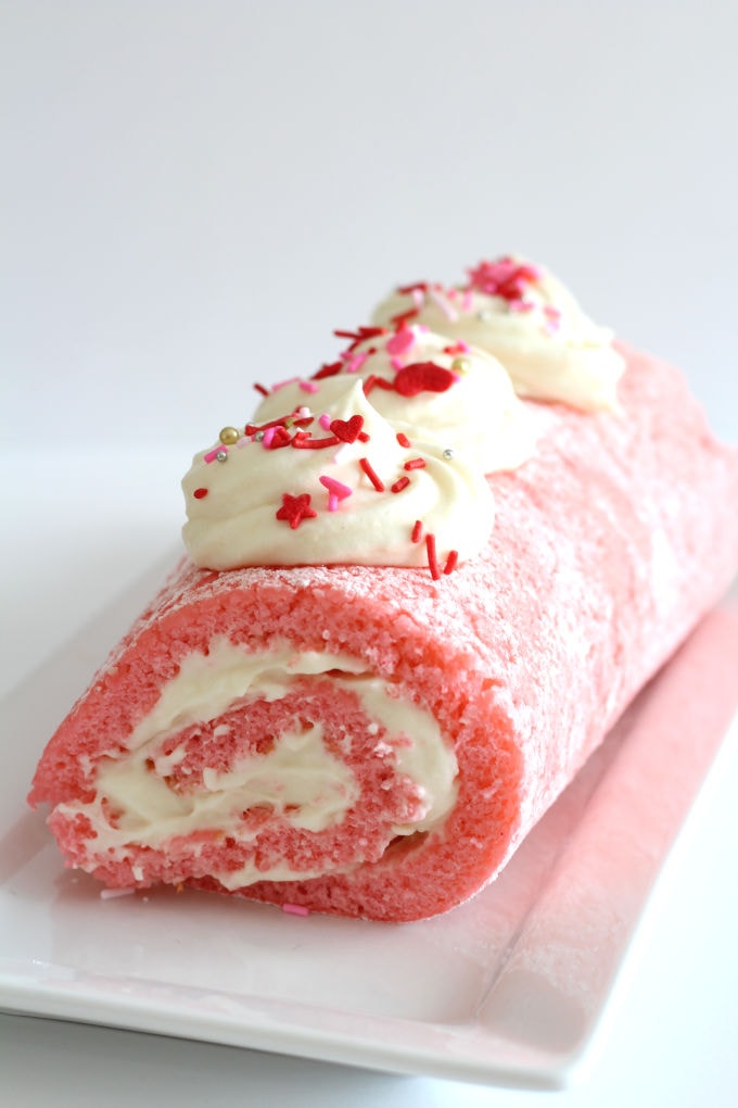 Pink roll cake with whipped cream and sprinkles on top.
