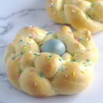 Italian Easter Bread wreath with a blue dyed egg in the middle. Colourful sprinkles are scattered all over the wreath.
