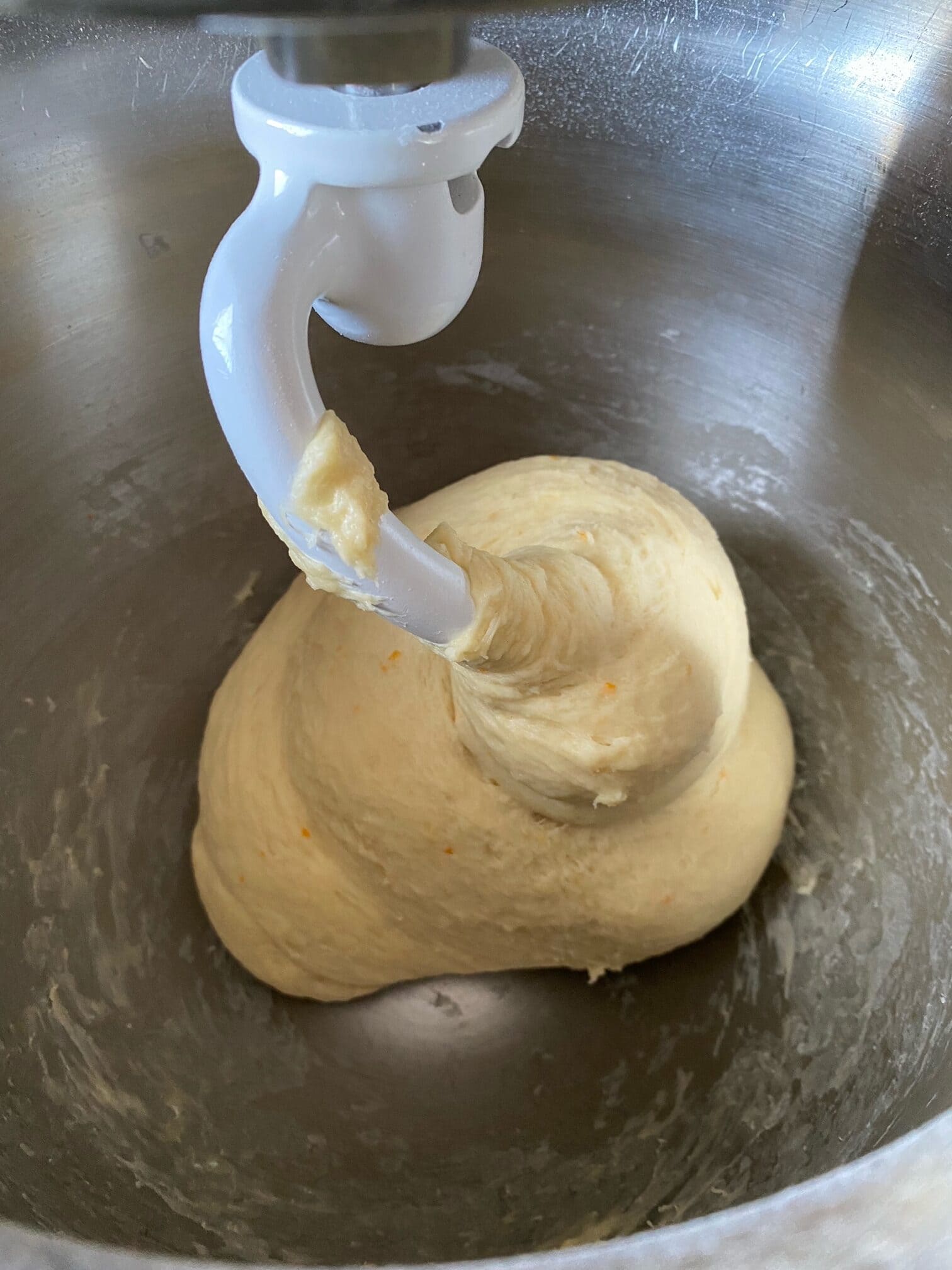 Italian Easter bread dough in a aluminum bowl of a stand mixer, with the dough hook attachment.
