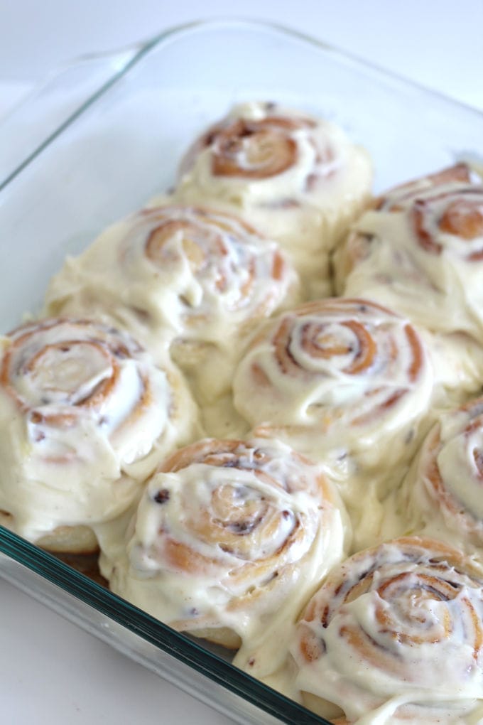 A baking dish full of cinnamon rolls with cream cheese topping.