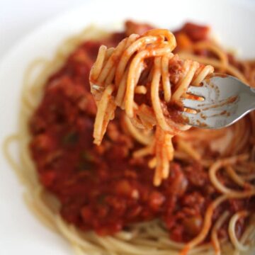 Spahgetti and meat sauce on a plate with a forkful of spaghetti on a fork.