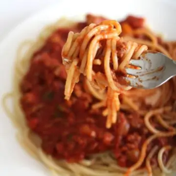 Spahgetti and meat sauce on a plate with a forkful of spaghetti on a fork.