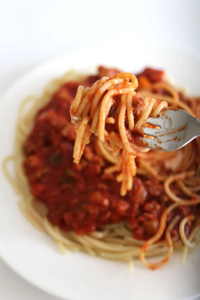 A forkful of spaghetti and meat sauce with a plate of it in the background.