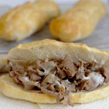 A philly cheesesteak with extra buns behind it.