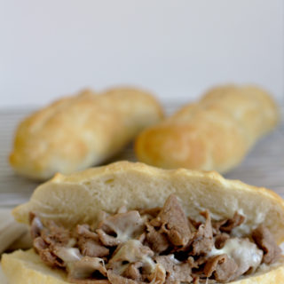 A philly cheesesteak with more buns in the background.