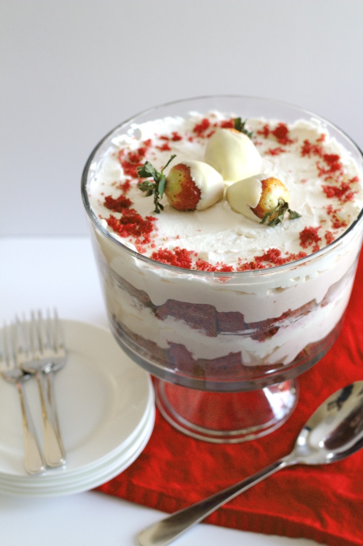 A red velvet cheesecake trifle with a serving spoon, plates and forks beside it.