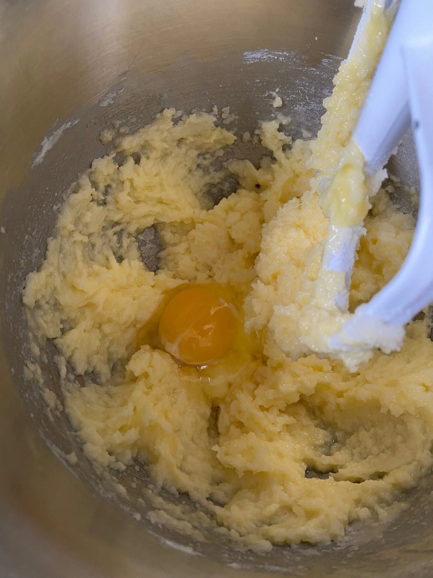 Cake batter and an egg in a large bowl of a stand mixer that is fitted with the beat attachment.