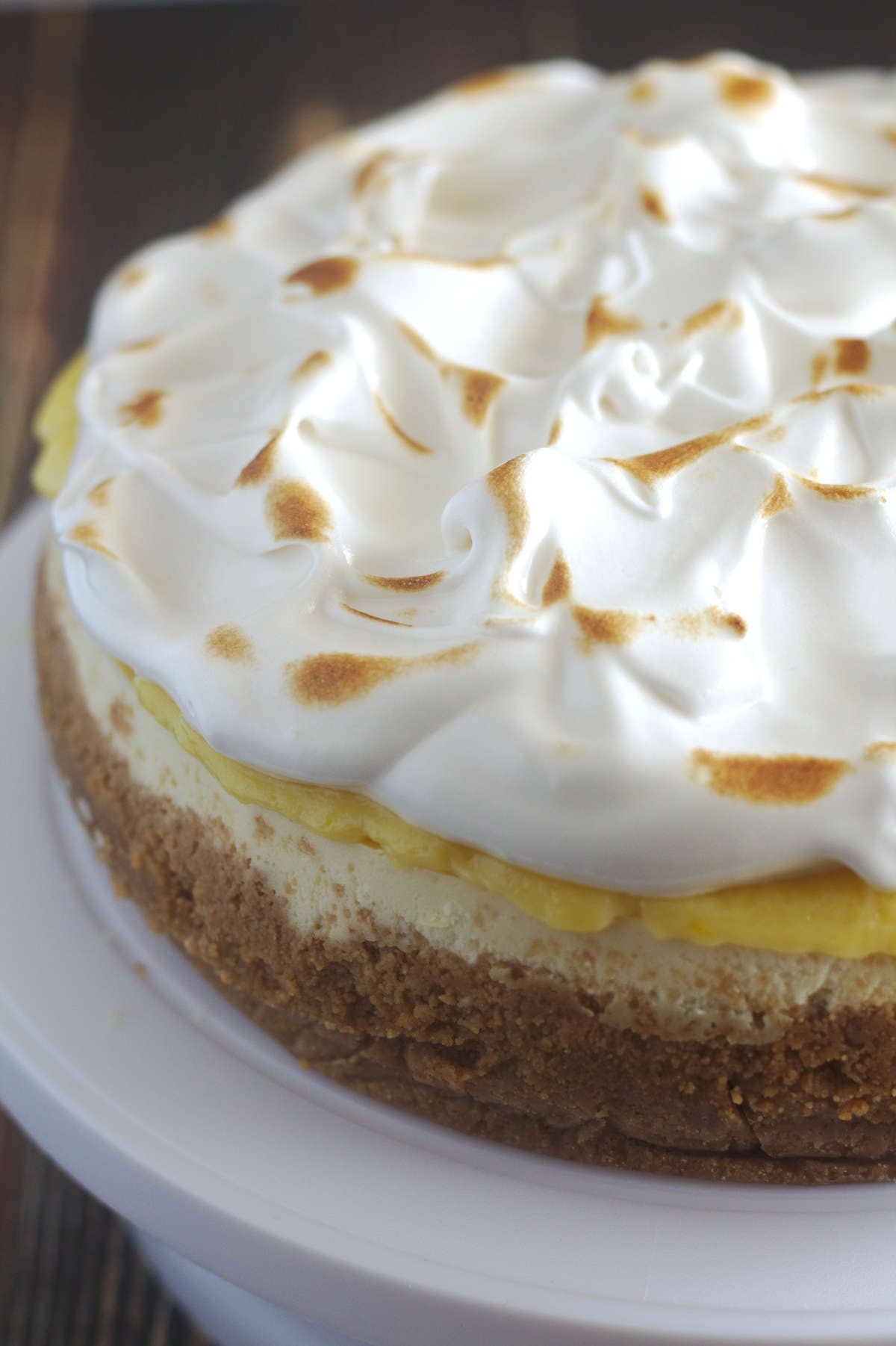 A partial view of a lemon meringue cheesecake on a white cake stand.