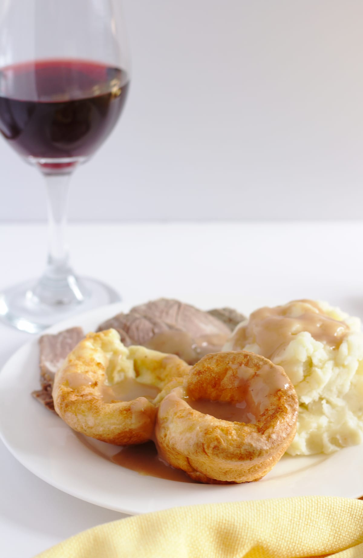 A plate of roast beef, mashed potatoes and Yorkshire pudding with a glass of red wine in the background.
