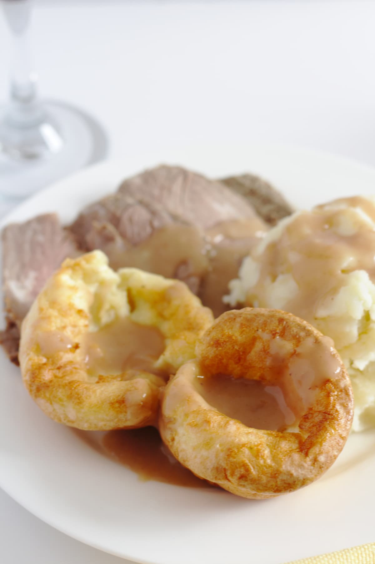 A plate of roast beef, mashed potatoes and Yorkshire pudding with a glass of red wine in the background.