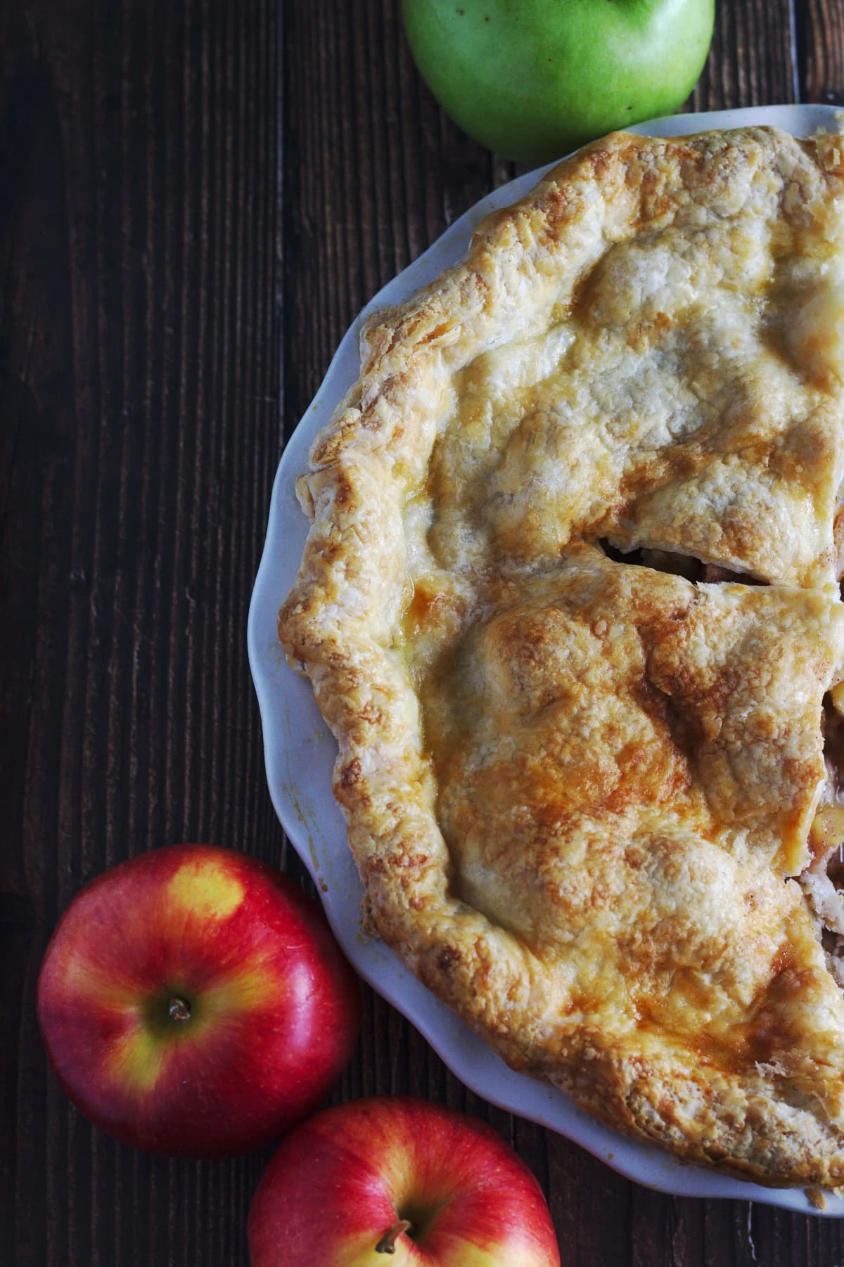 A pie in a pie shell surrounded by apples. 