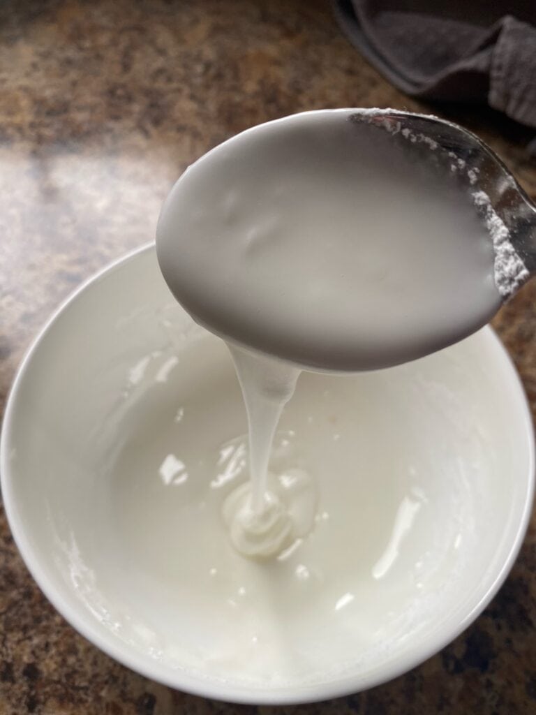 The glaze in a bowl with a spoon showing the consistency of it.