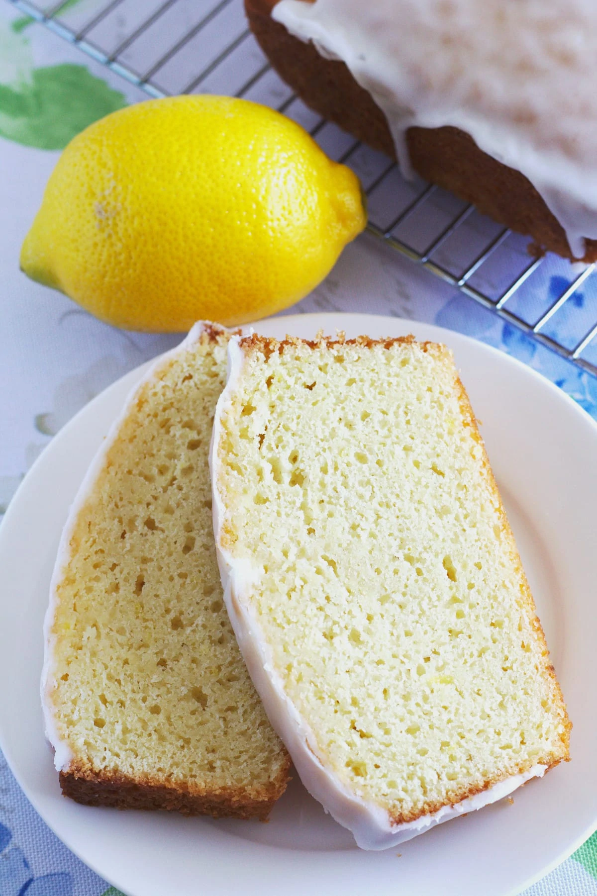 Two slices of lemon loaf on a plate with a lemon and the rest of the loaf.