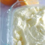 Sherbet in a container with cut oranges in the background.