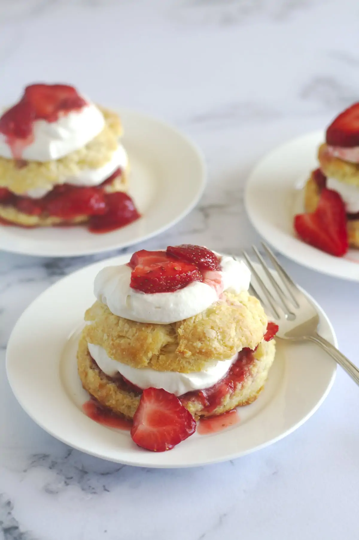 A strawberry shortcake on a plate with a fork.  Other plated strawberry shortcakes are in the background.