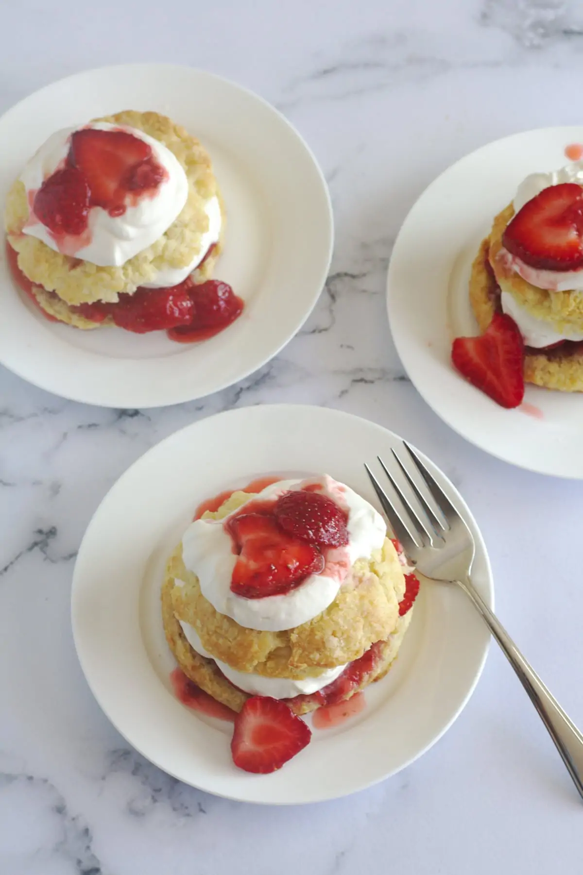 An above view of strawberry shortcakes on plates.  The bottom one has a fork on the plate.