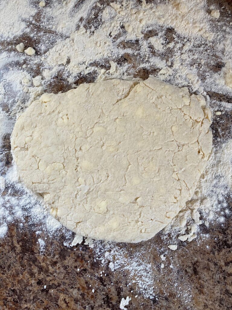 Biscuit dough formed and patted down on a floured bench.