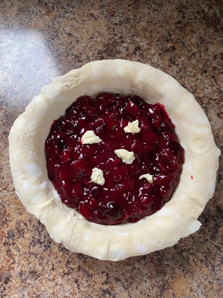 Cherry pie filling in the pie crust with butter dotted on top.