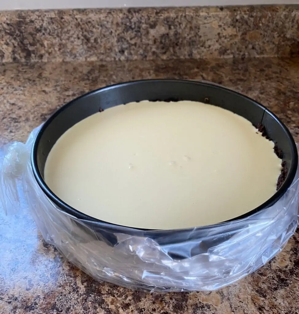Aluminum foil lines the outside of the springform pan, and a crock pot liner is tied around it.