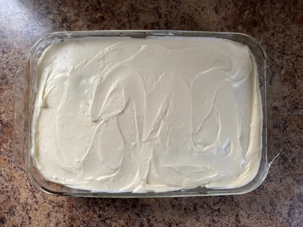 Cream cheese frosting spread over the cake in a baking dish.
