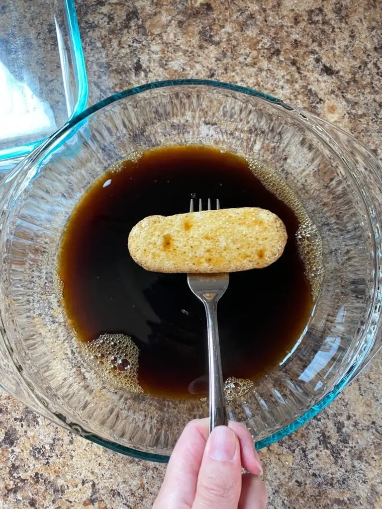 Coffee and coffee liquor in a bowl with a ladyfinger on a fork above it.