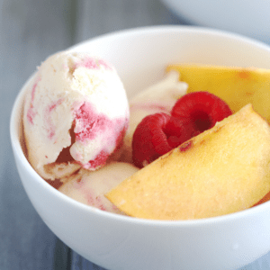 Ice Cream in a white bowl with raspberries and peaches.