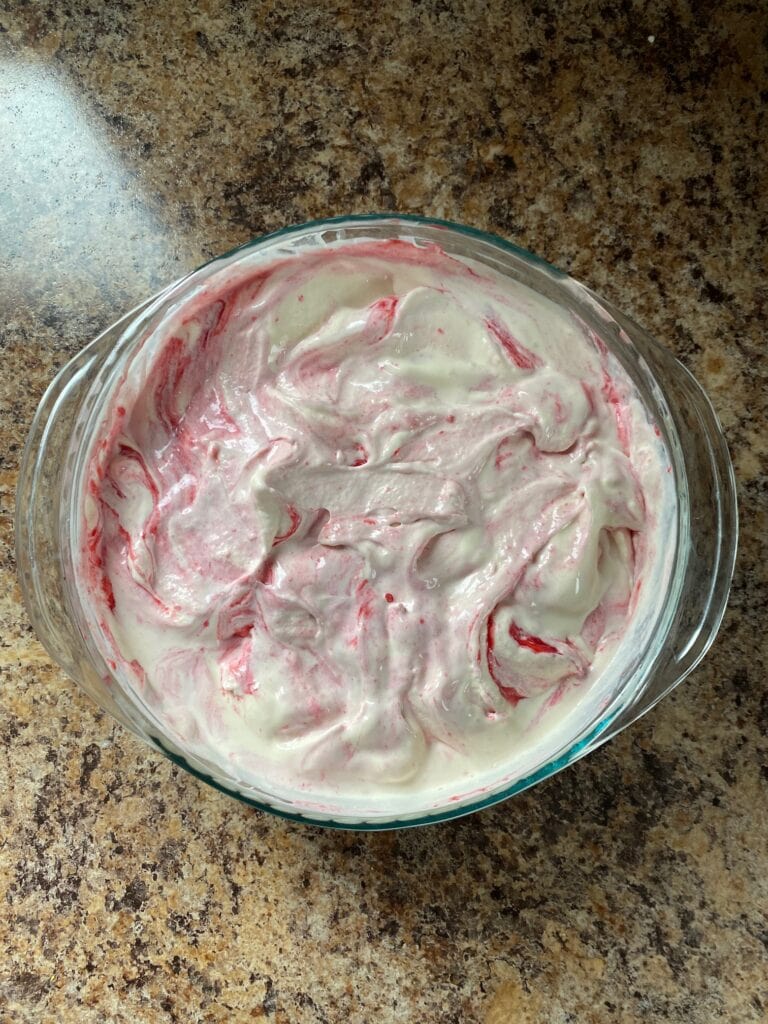 Raspberry sauce swirled through ice cream in a large clear bowl.