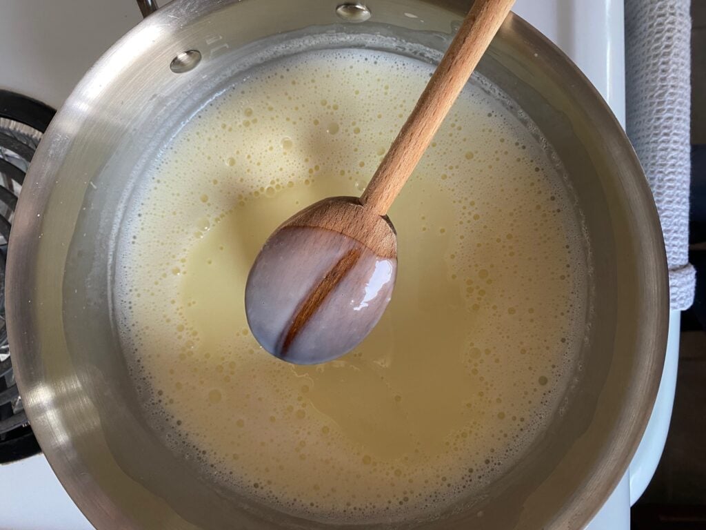 Custard in a saucepan with a wooden spoon with a line through it showing the custard is cooked.