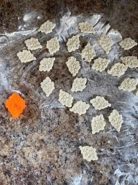 Leaf pastry decorations scattered on a floured work surface.  An orange cookie cutter sits to the left.