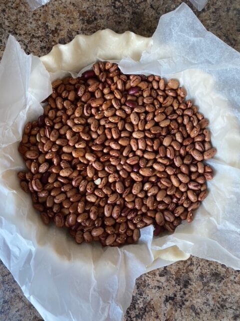 Pie shell with parchment paper over it and filled with baking beans.