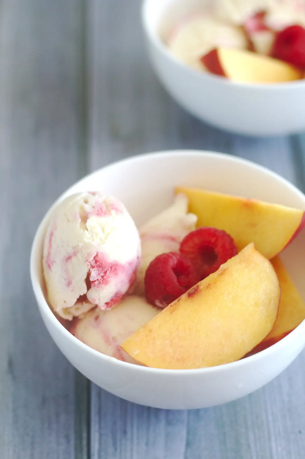 Ice cream in a white bowl with raspberries and peaches.