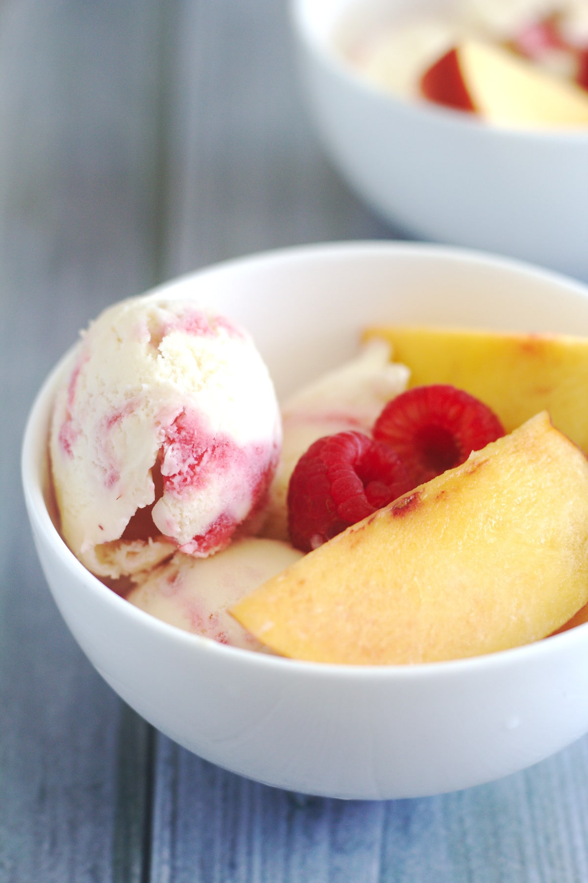 Ice cream in a white bowl with raspberries and peaches.