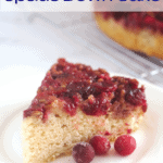 A slice of cake on a white plate with three whole cranberries in front of it.