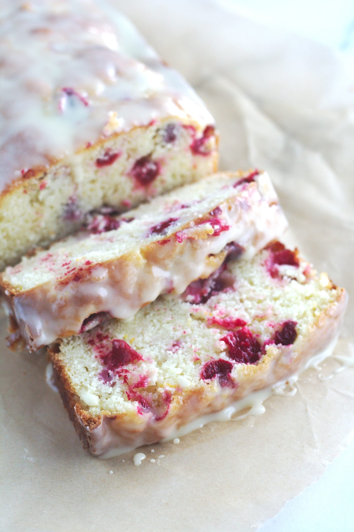 Cranberry orange bread on a piece of parchment paper.  A few slices of bread has been sliced.