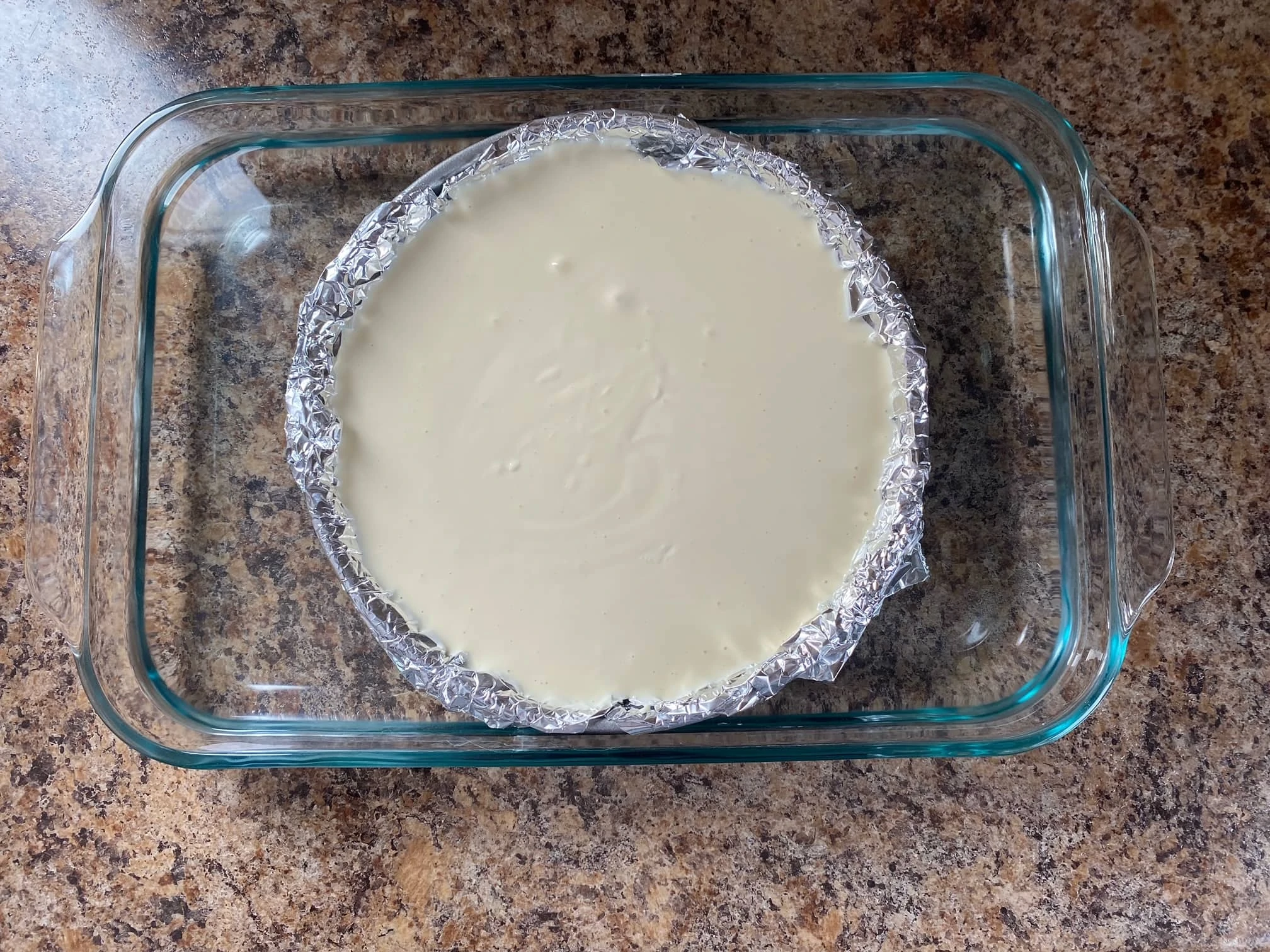 Cheesecake in a foil lined cake pan.  The cheesecake pan is sitting inside a large baking dish with water around it.