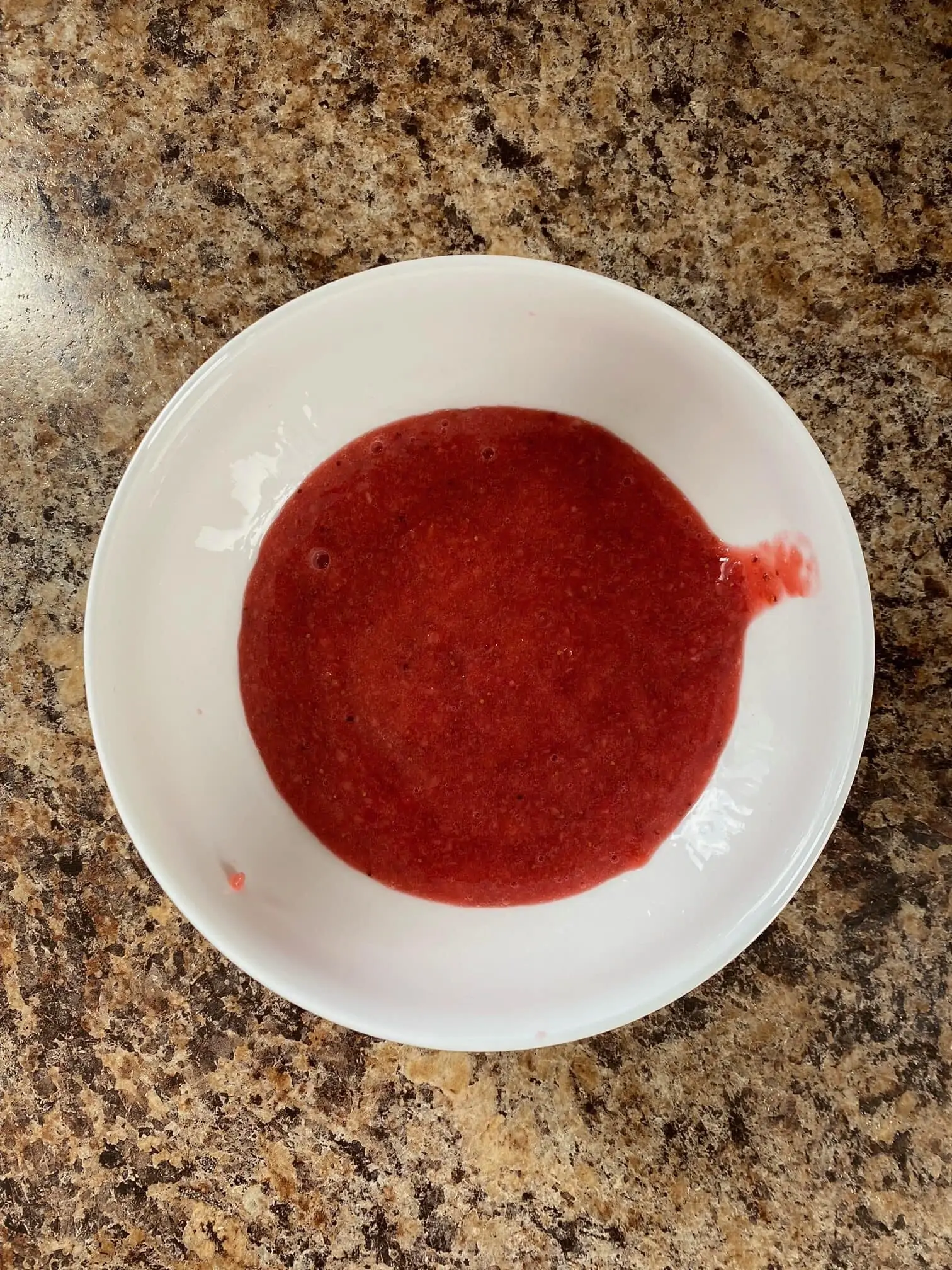 A small white bowl with strawberry sauce in it.