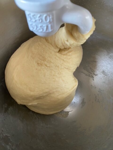 Kneaded cinnamon roll dough in a stand mixer fitted with the dough hook attachment.