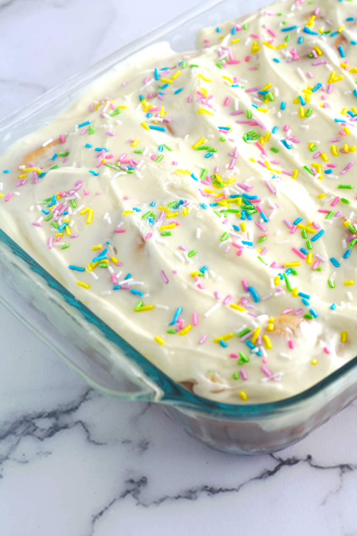 A large clear pan filled with cinnamon rolls.  Frosting and sprinkles are on top.