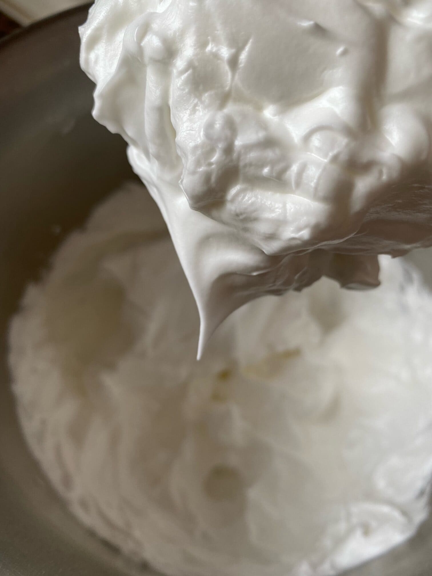 Meringue topping in a large mixing bowl.  Some topping is on a wire whisk.