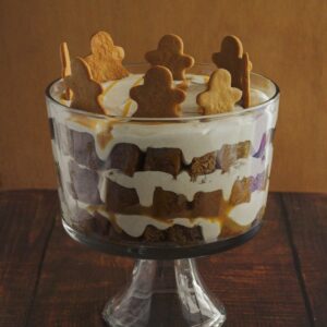 A trifle in a clear trifle dish. Gingerbread men decorate the tip of the trifle.